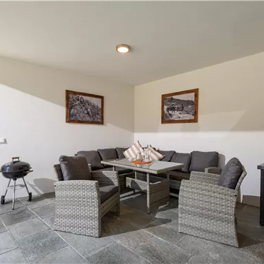 A cozy terrace with modern furniture and a table. In the background, some decorative pictures are visible on the wall.