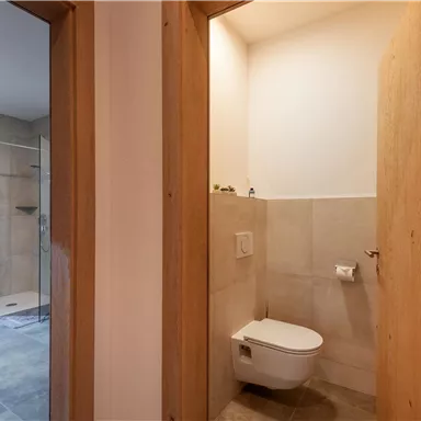 A modern bathroom with a shower and a toilet. Bright tiles and wooden panels create a pleasant atmosphere.