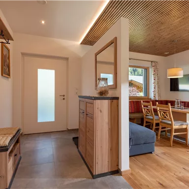 A cozy entrance area with wooden shelves and a bench. The room leads to a dining area with a table and chairs.