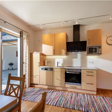 A modern kitchen with wooden cabinets and an open connection to the dining area. The space is brightly lit and has large windows that provide a view of the outdoors.