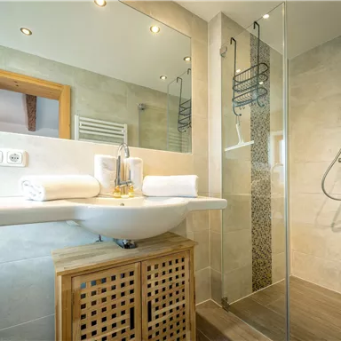 Ein modernes Badezimmer mit einer Dusche und einem Waschbecken. Es sind Handtücher und helle Fliesen zu sehen.