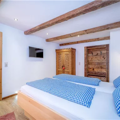 Ein gemütliches Schlafzimmer mit zwei Betten und blauen Kissen. Holzbalken an der Decke und rustikale Möbel schaffen eine einladende Atmosphäre.
