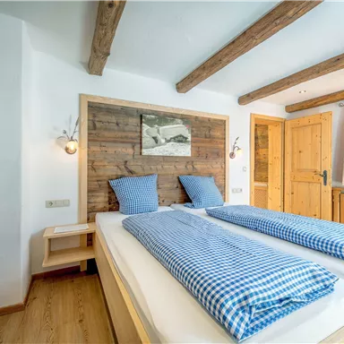 Ein gemütliches Schlafzimmer mit einem Doppelbett und blau-weiß karierten Bettdecken. Die Wände sind aus Holz, und es gibt große Fenster mit viel natürlichem Licht.