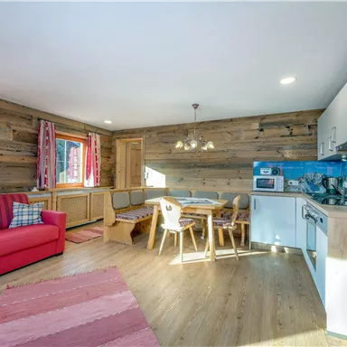 Ein gemütlicher Wohnraum mit einem roten Sofa, einem Esstisch und einer modernen Küche. Die Wände sind mit Holz verkleidet und es gibt zwei Fenster, die viel Licht hereinlassen.
