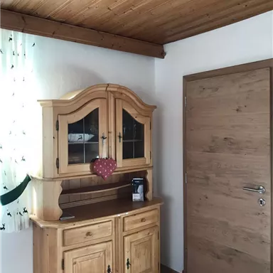 A cozy room with a wooden cabinet and a door. The cabinet has glass doors and a heart-shaped decoration.