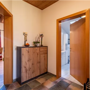 Ein heller Flur mit Holzdetails und einem modernen Kommode. Durch die Türen ist der Zugang zu weiteren Räumen sichtbar.