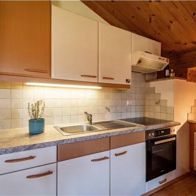 Eine moderne Küche mit Holzdecke und hellen Schränken. Es gibt ein Spülbecken, einen Herd und verschiedene Küchengeräte.