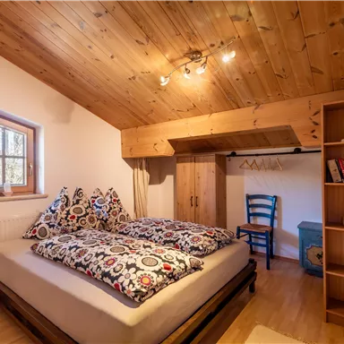 Ein gemütliches Schlafzimmer mit einem Holzdach und einem großen Bett. Ein Schreibstuhl und ein Regal ergänzen den Raum.