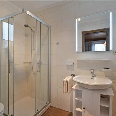 A modern bathroom with a glass shower cabin and a sink. Bright tiles and a large mirror lighting create a pleasant atmosphere.