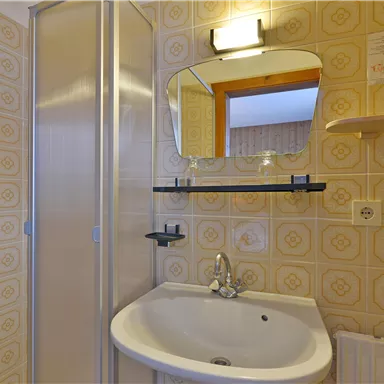 A small bathroom with a shower, a rectangular sink, and a mirror. The walls are decorated with yellow tiles.