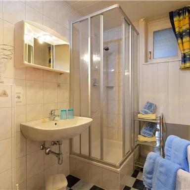 Ein modernes Badezimmer mit einer Dusche, einem Waschbecken und einem großen Spiegel. Handtücher sind ordentlich auf einem Regal angeordnet.
