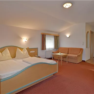A cozy hotel room with a double bed, sofa, and television. The decor is friendly and brightly designed.