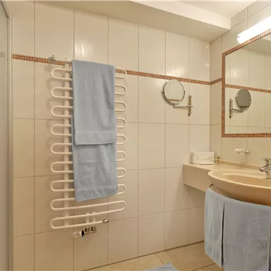 A modern bathroom with bright tiles and a shower. Towels in soft shades of blue hang on a towel warmer.