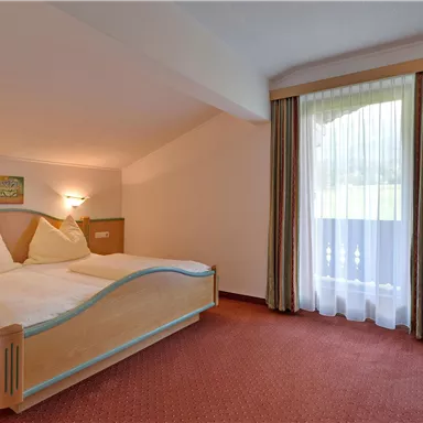 A cozy bedroom with two beds and soft lighting. The window offers a view of a green landscape.