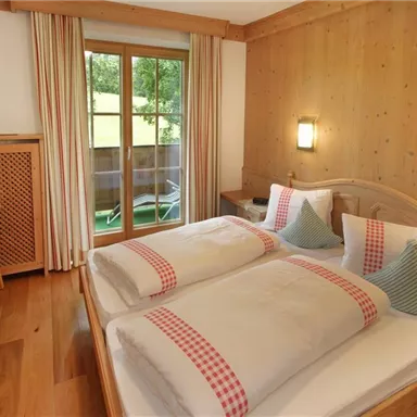 A cozy bedroom with two single beds and wooden-paneled walls. The room features a small table and access to a balcony.