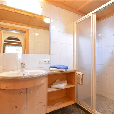 Ein modernes Badezimmer mit Holzregalen und einer Dusche. Die Wände sind hell gefliest und es gibt einen runden Waschbecken.