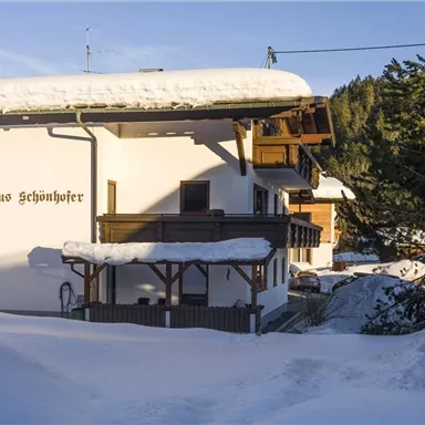 A cozy house in the snow with a covered balcony.  
Surrounded by a snowy landscape and trees.