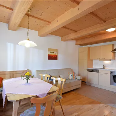Eine helle und moderne Küche mit Holzbalkendecke. Es gibt einen Essbereich mit einem Tisch und einer gemütlichen Sitzecke.
