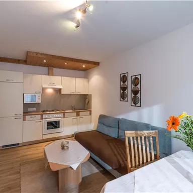 Eine moderne Wohnung mit einer offenen Küche und einem gemütlichen Wohnbereich. Auf dem Tisch steht eine Vase mit bunten Blumen.