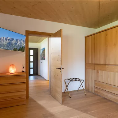 A modern bedroom with wooden decor and a large window. A television hangs on the wall and a softly glowing salt crystal rests on the nightstand.