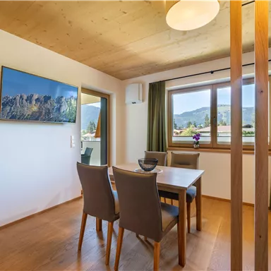 A modern dining room with a table and chairs. Through the window, you can see a beautiful view of the mountains.
