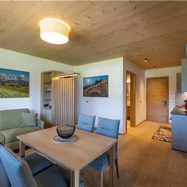 A modern living room with a dining area and a cozy sofa corner. Pictures of landscapes hang on the walls, and the kitchen is well-equipped.