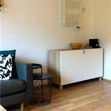 A modern living room with a gray sofa and a side table. On the opposite side stands a white cabinet and a decorative basket.