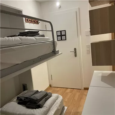 A simple room with a loft bed and stacked towels. The walls are bright, and the room contains a desk and chair.