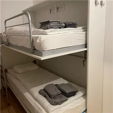 A simple bedroom with a loft bed and a bed underneath. Both beds are neatly made with bedding and towels.
