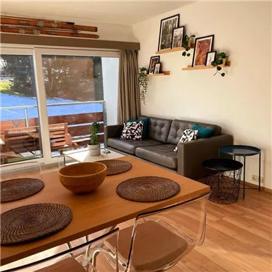 A modern living room with a comfortable sofa and a dining table.
Large windows offer a view of a terrace with garden furniture.