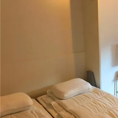 A simple room with two single beds and white bedspreads. The walls are bright and designed in a minimalist style.