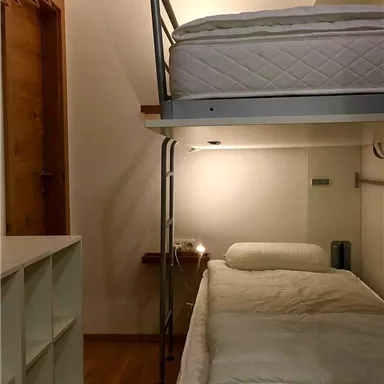 A simple bedroom with a bunk bed and a desk. The floor is wooden, and there is a wardrobe on the wall.