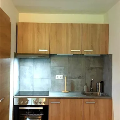 A modern kitchen with wooden cabinets and gray walls. The stove and sink are well arranged, and the space feels bright and inviting.