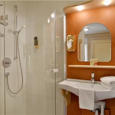 Ein modernes Badezimmer mit einer Duschkabine und einem Waschbecken. Weiße Handtücher sind ordentlich auf dem Waschbecken gestapelt.