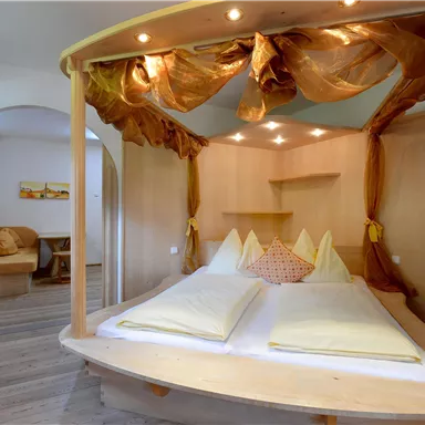 Ein gemütliches Schlafzimmer mit einem Holzbett und weichen Kissen. Die warme Beleuchtung und die dekorativen Vorhänge schaffen eine entspannte Atmosphäre.