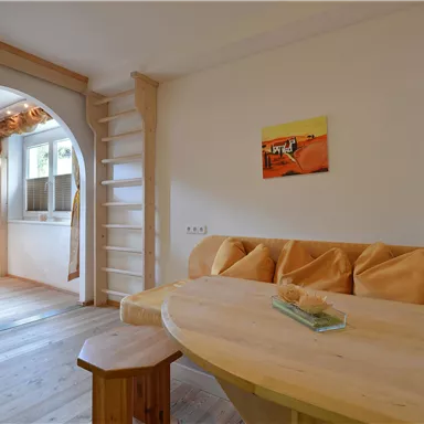 Ein gemütlicher Innenraum mit Holzdetails und einer runden Sitzecke. An der Wand hängen einige Bilder, und es gibt eine kleine Treppe im Hintergrund.