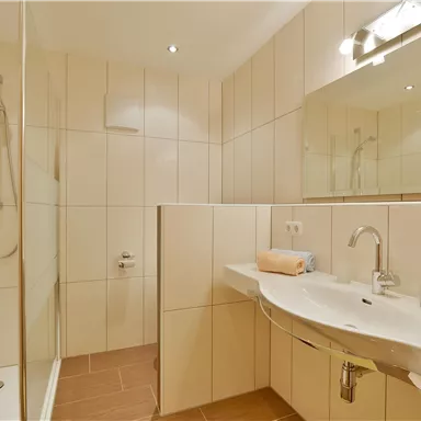 A modern bathroom with a shower and bright tiles. On the sink, there is a towel and an orange towel.