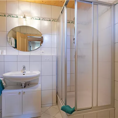 A modern bathroom with a shower cubicle and a sink. The walls are tiled and decorated with green towels.