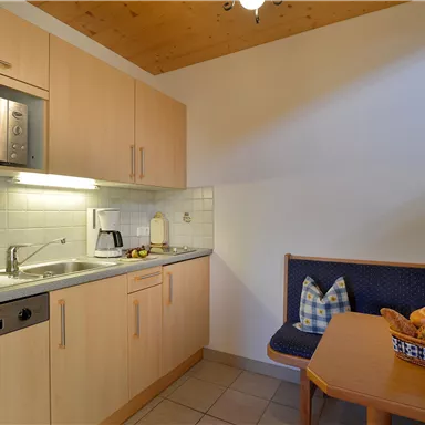 A bright kitchen with modern appliances and wooden details. A table with fresh fruit and a cozy seating area is also present.