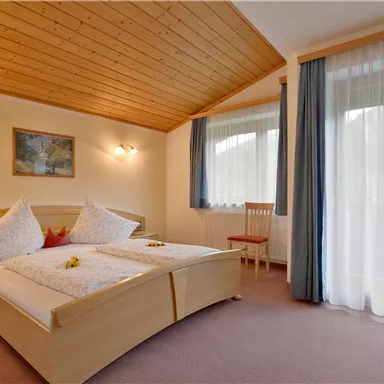 A comfortable bedroom with two beds and a wooden ceiling. Large windows provide plenty of daylight and a cozy atmosphere.