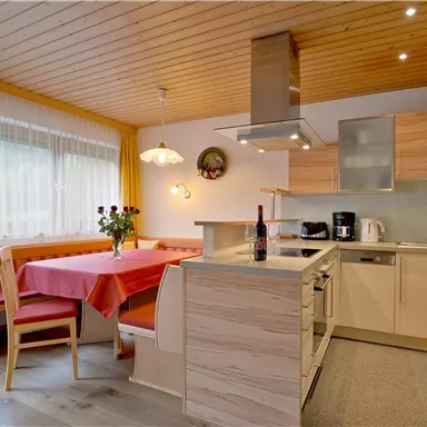 A modern kitchen with wood paneling and bright colors. The table is set with a red tablecloth and there are fresh flowers on the table.