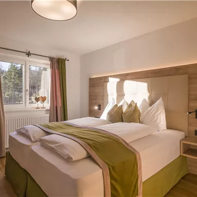 A modern bedroom with a comfortable double bed and bright colors. The window offers a view of nature, and the curtains add warmth to the room.