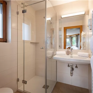 A modern bathroom with a glass shower and a sink. Bright tiles and a large mirror create a friendly atmosphere.
