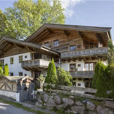 Ein traditionelles alpenländisches Haus mit Holzverkleidung und großzügigen Balkonen. Umgeben von grünen Bäumen und einem gepflegten Garten.