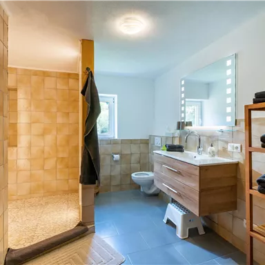 A modern bathroom with a large shower and a wooden washbasin. There are bright tiles and towels on a shelf.