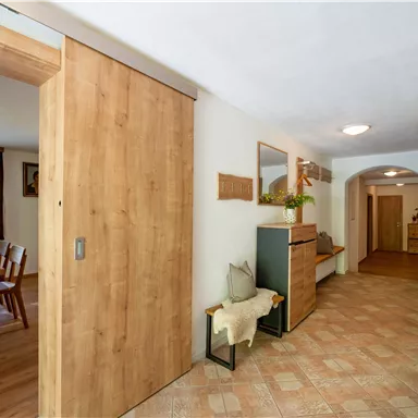 A bright hallway with wooden details and an inviting ambiance. On the left side, there is a dining table and on the right a coat rack.