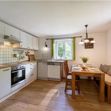 A modern kitchen with white cabinets and wooden flooring. A dining area with a wooden table and comfortable seating is also available.