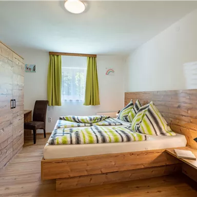 A cozy bedroom with a double bed and wooden paneling. The windows are adorned with green curtains, and there's a desk in the corner.