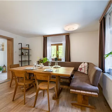 A cozy dining area with a large wooden table and seating. Natural light enters the room through large windows.