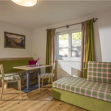 A cozy living space with a table and chairs as well as a comfortable seating area. The ambiance is bright and friendly, enhanced by green and pink accents.